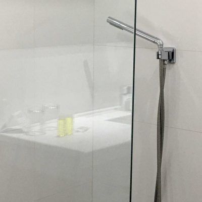 Showerhead attached to a glass shower door in a modern white bathroom.