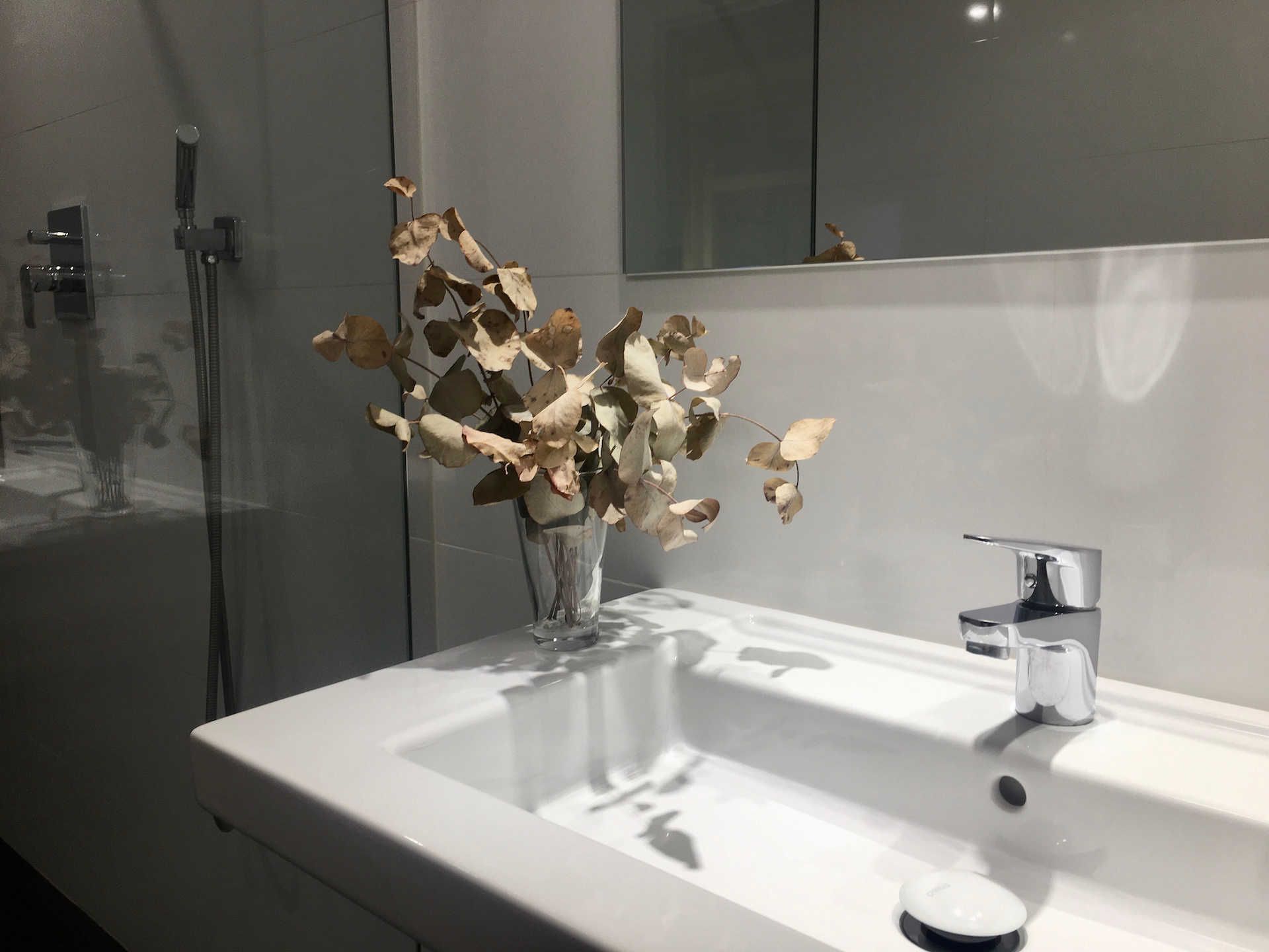 White bathroom sink with faucet and dried floral arrangement in a vase.
