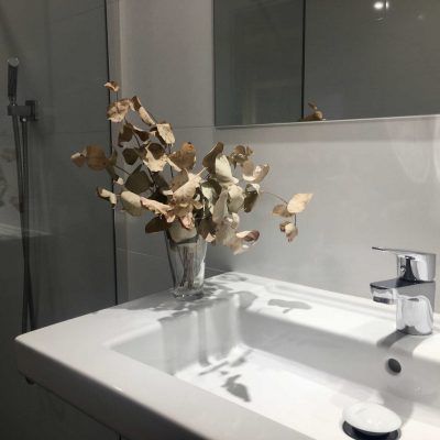 White bathroom sink with dried floral arrangement, chrome faucet, and mirror.
