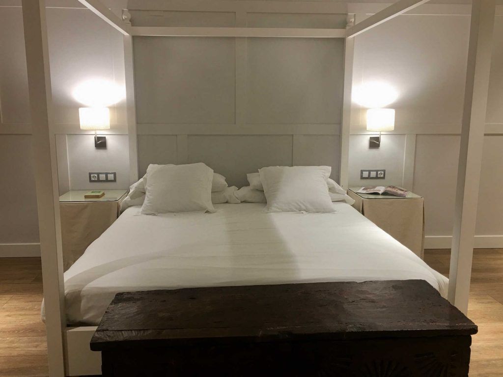 Bedroom with a white canopy bed, two bedside tables, and a wooden chest. Two wall lamps are mounted above the bed.