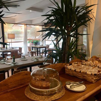Restaurant interior with tables set for dining, plants, and a bread basket.
