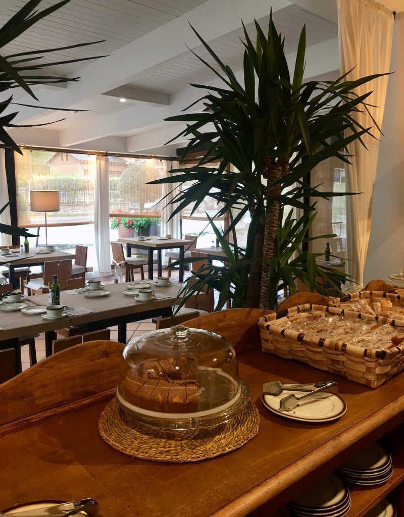 Buffet counter with cake, baskets, and dishes in a bright, airy restaurant. Palm trees and tables in the background.