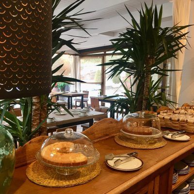 Breakfast buffet: Cake, bread, and pastries on a wooden counter with a dining area in the background.
