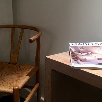 Wooden chair beside a wooden side table with a magazine on top, all against a neutral wall.