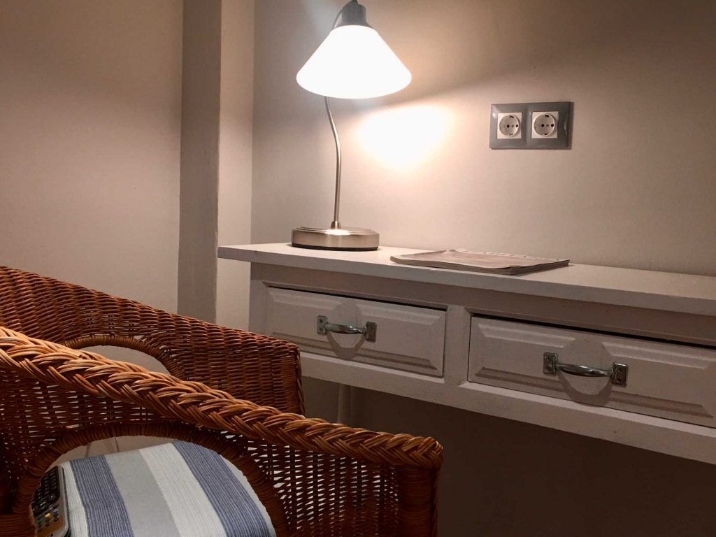 Wicker chair next to a white console table with a lamp and electrical outlets on the wall.