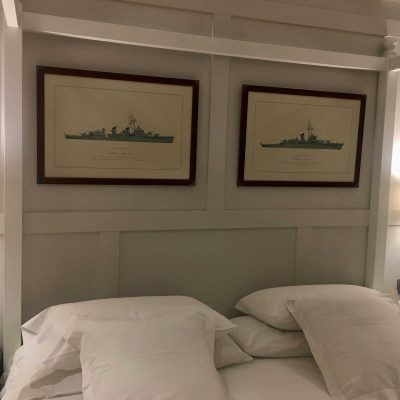 Two framed ship diagrams hang above a bed with white bedding and pillows.