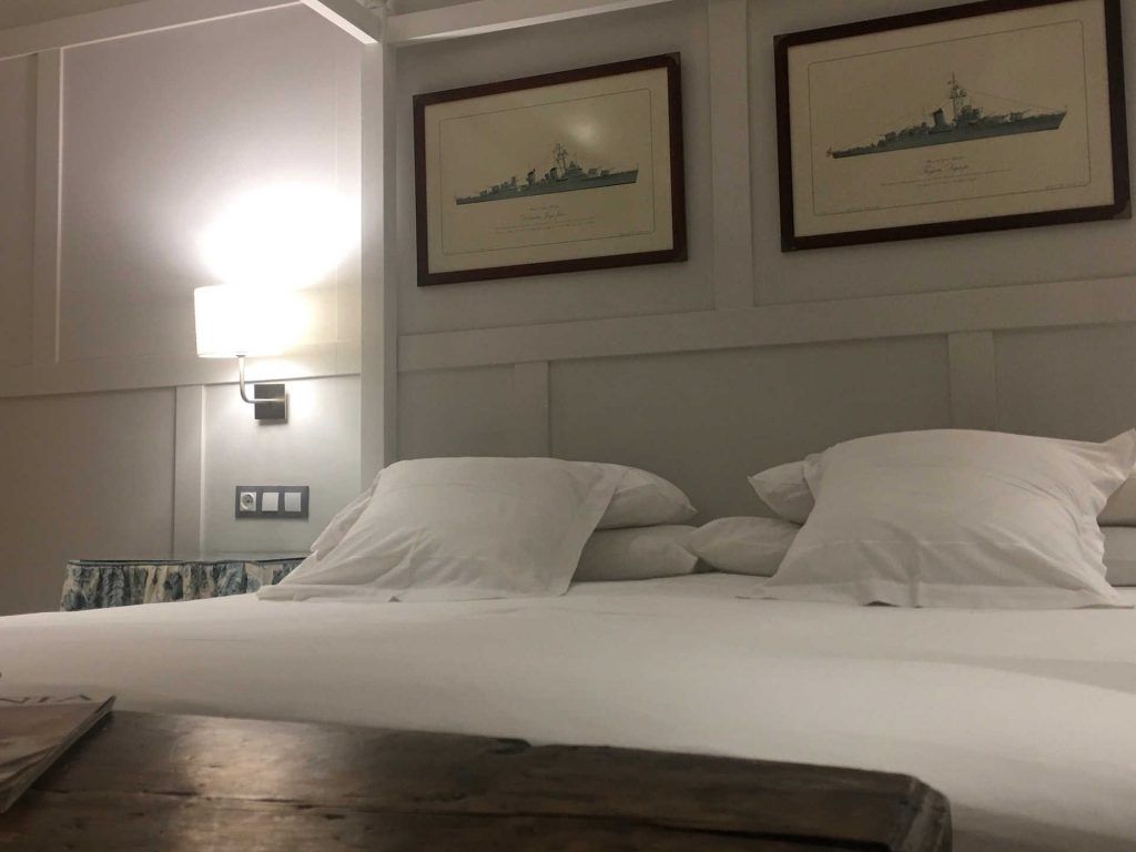 Bedroom with white bedding, pillows, art, and a bedside lamp.