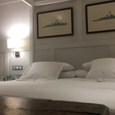White bed with pillows, two framed prints, and a wall-mounted lamp.