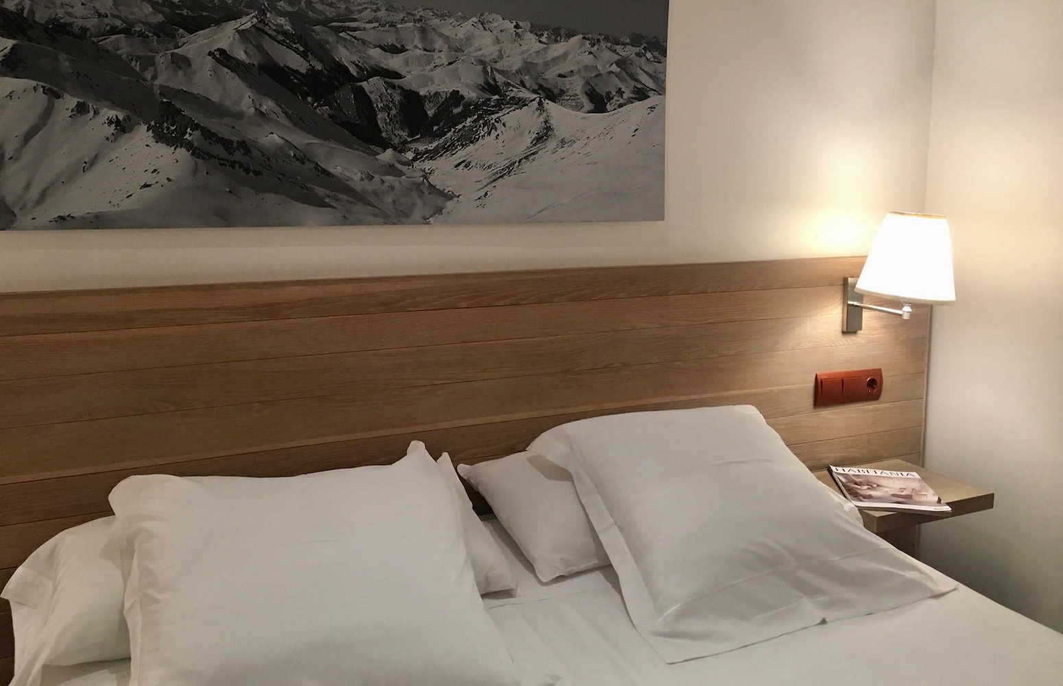 Bedroom with a bed, white pillows, a lamp, a mountain landscape artwork above the headboard.