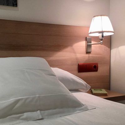 Bedroom with white bedding, wooden headboard, wall-mounted lamp, and nightstand.