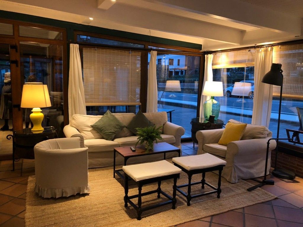 Cozy living room with cream sofas, beige rug, lamps, and a view of the street through large windows.