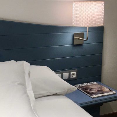 Blue headboard with white bedding, lamp, and magazine.