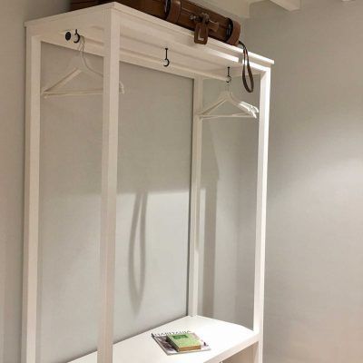 White wooden coat rack with luggage on top and hangers.