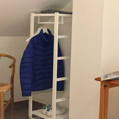 White coat rack with blue jacket and shoes inside a room.