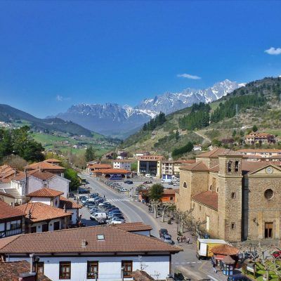 Townscape with buildings, street, and mountains in the background under a blue sky.