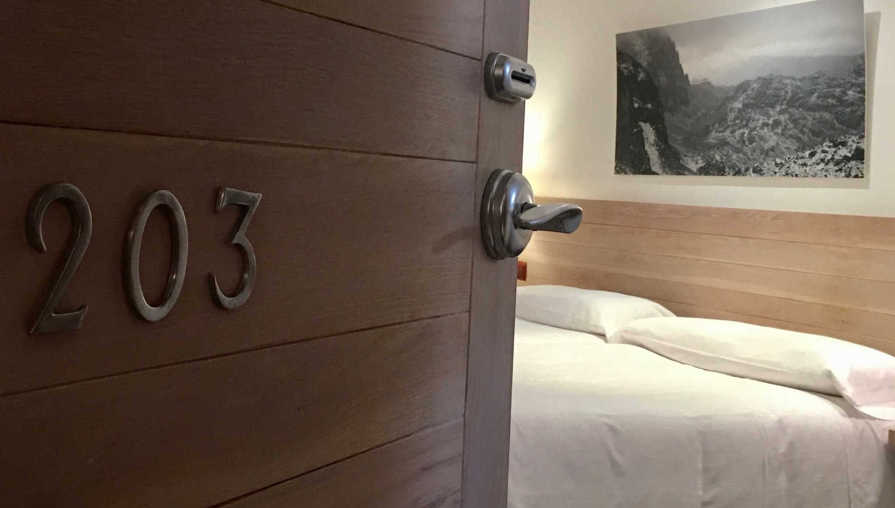 Hotel room door open, revealing a bed with white linens and a black and white photo on the wall. Number 203 on the door.