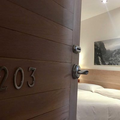 Hotel room door ajar; room number 203 visible; bed and artwork in the background.