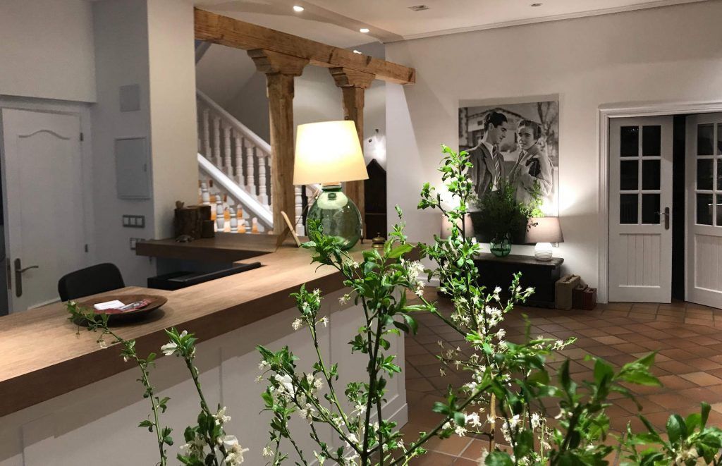 Reception area with wooden desk, plants, and staircase in the background. White walls, warm lighting.