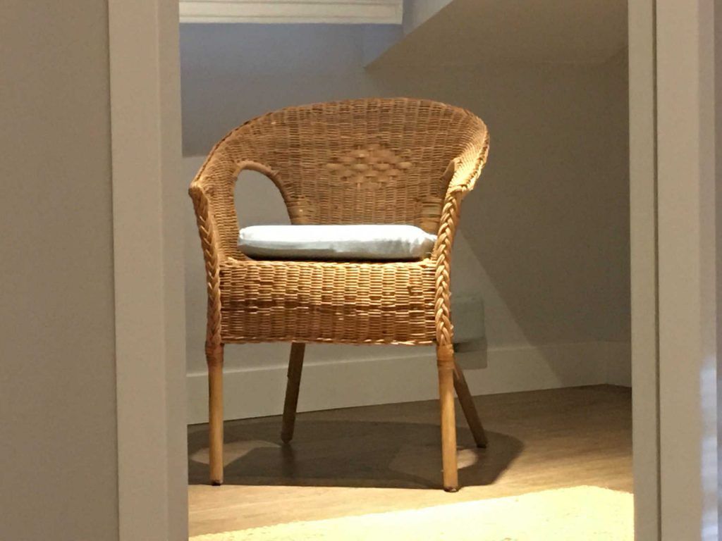 Wicker chair with light blue cushion inside a doorway, on a wooden floor.