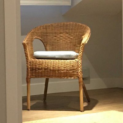 Wicker chair with light-colored cushion sits in a brightly lit alcove, with a wooden floor.