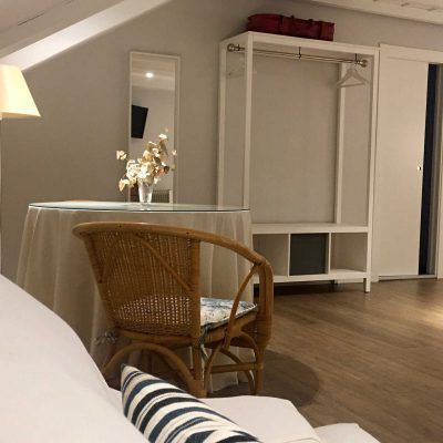 Bedroom with wicker chair, table with flowers, clothing rack, mirror, and white walls.