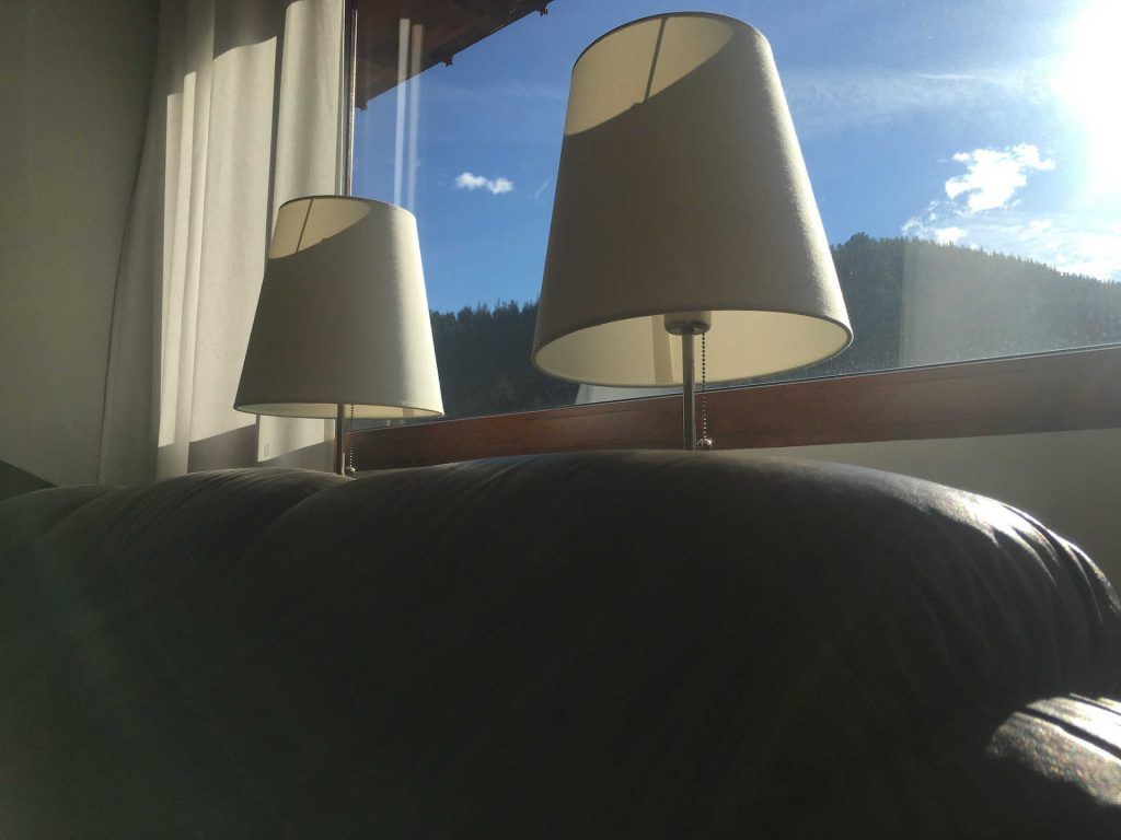 Two lamps on a sofa, in front of a window with a blue sky and mountain view.