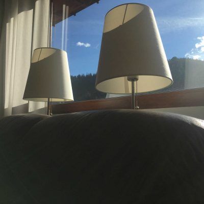 Two lamps with white shades sit on a dark couch; a bright sky is seen outside a window behind them.