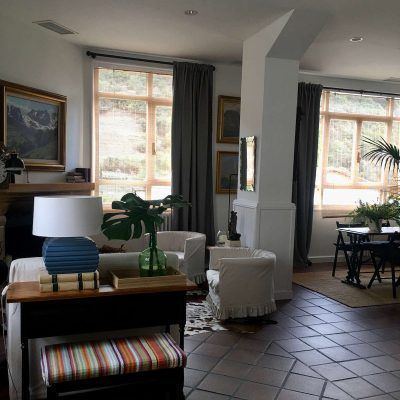 Living room with large windows, fireplace, white chairs, and potted plants.