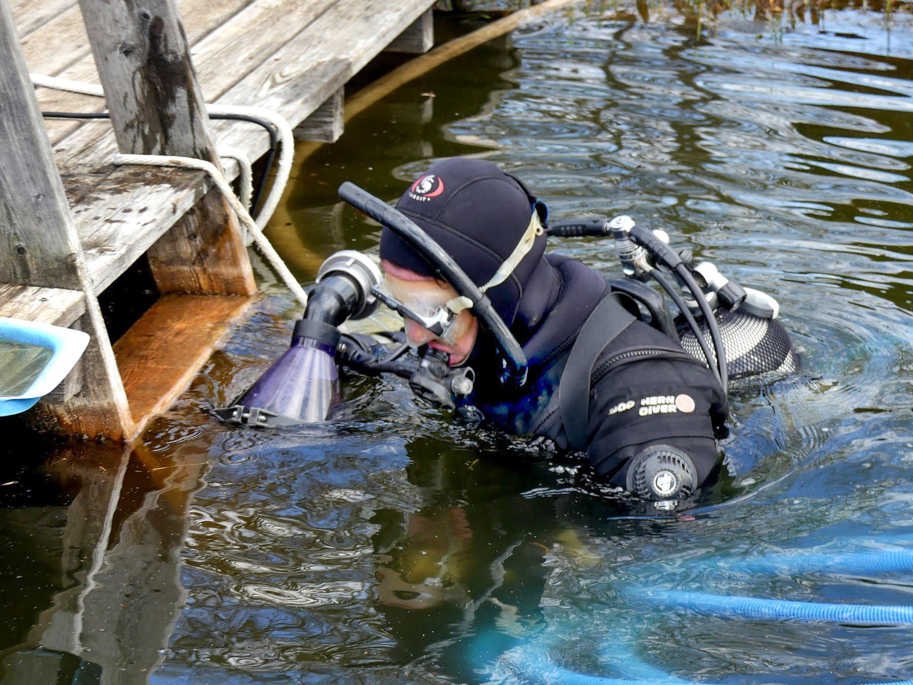 Taucher im dunklen Wasser in der Nähe eines Holzstegs, der ein Gerät hält.