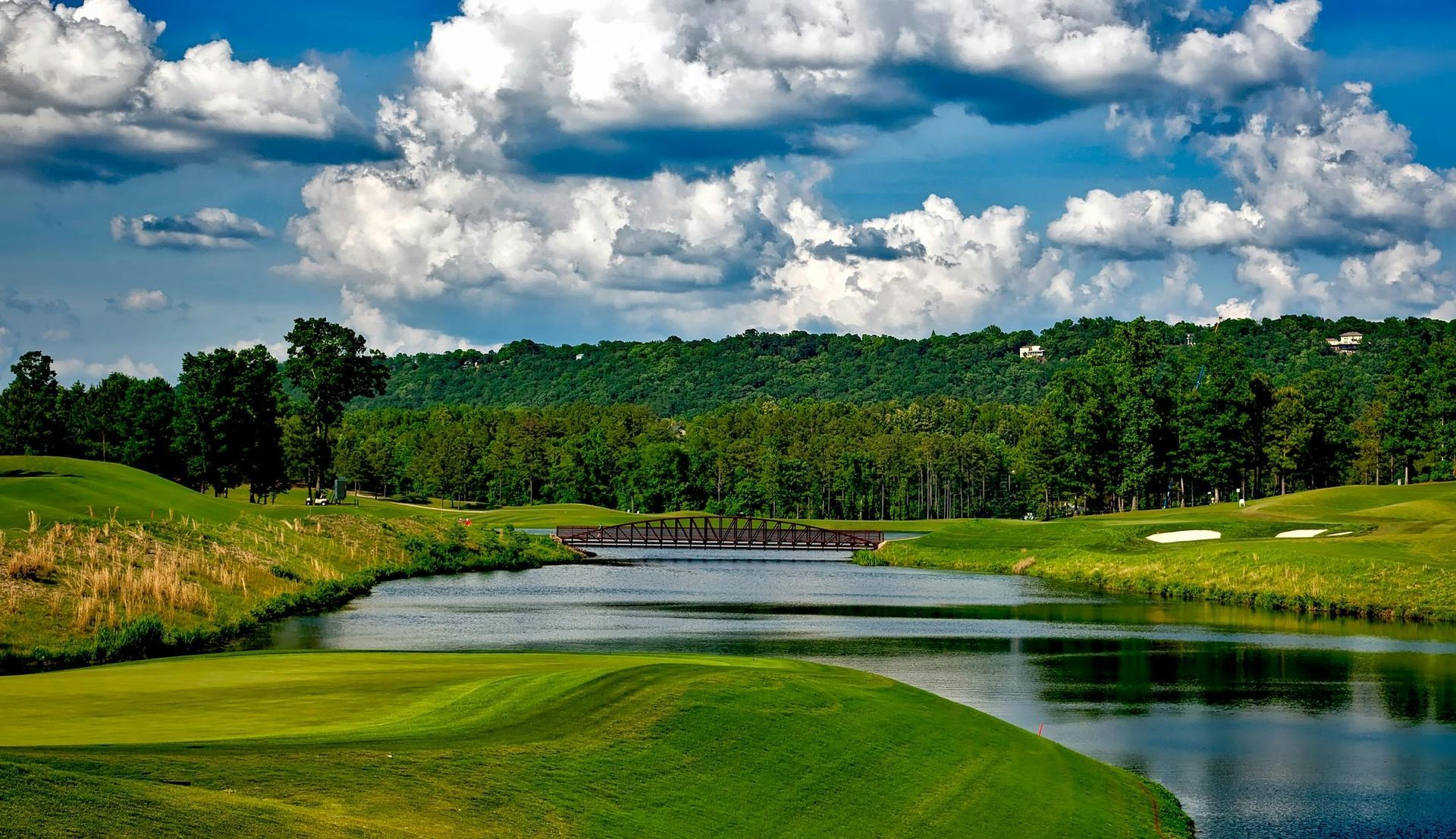 Malerischer Golfplatz mit Wasserspiel, üppig grünen Fairways und einer Brücke unter bewölktem Himmel.