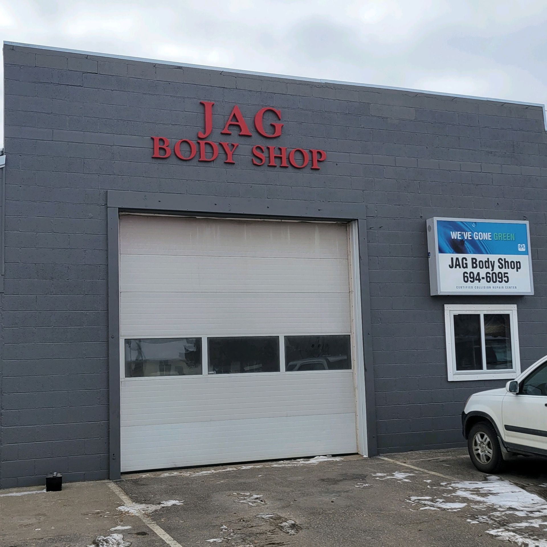 Gray JAG Body Shop building with a large garage door and parked white SUV outside