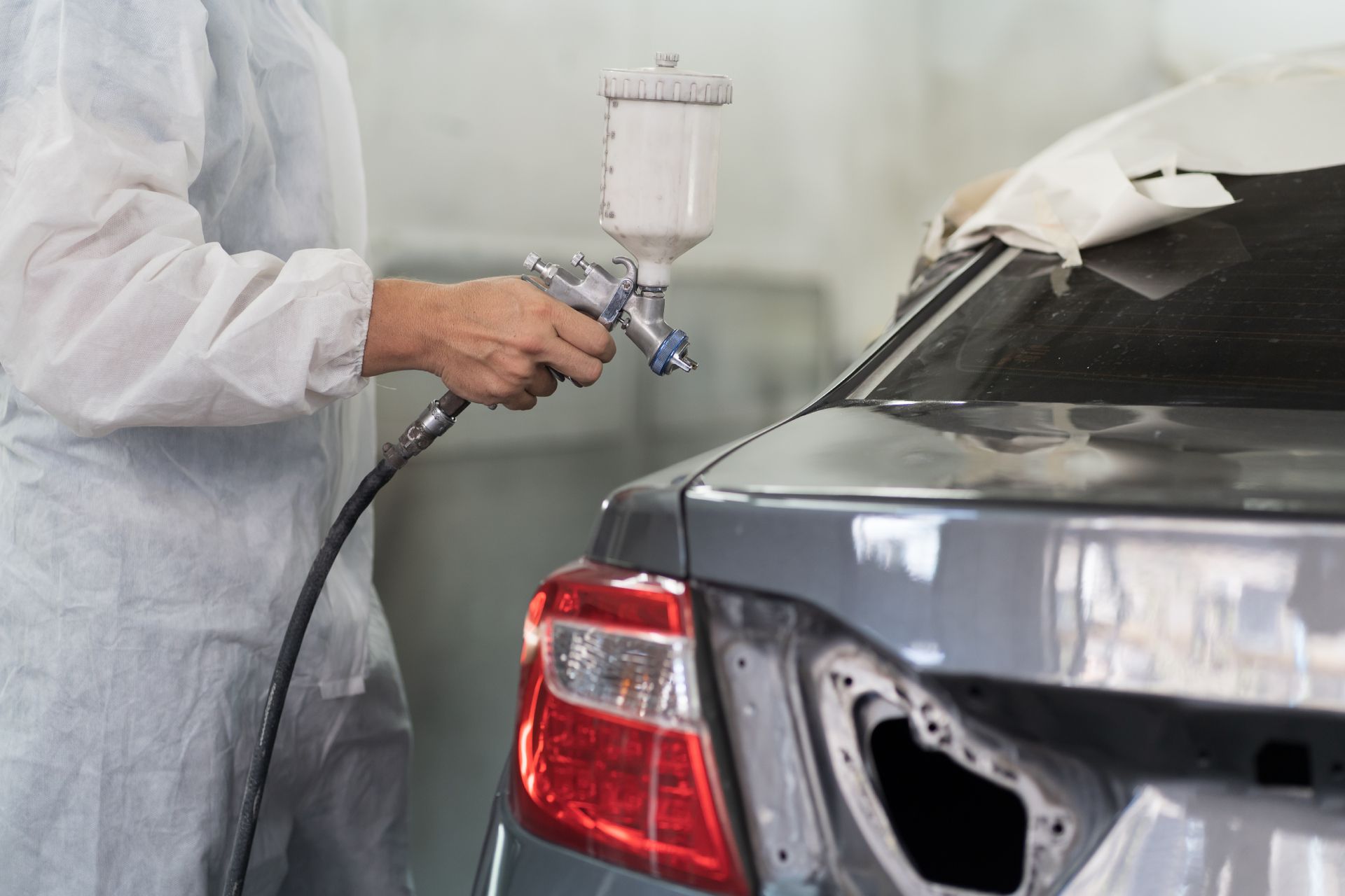Person spray-painting a gray car body in a workshop