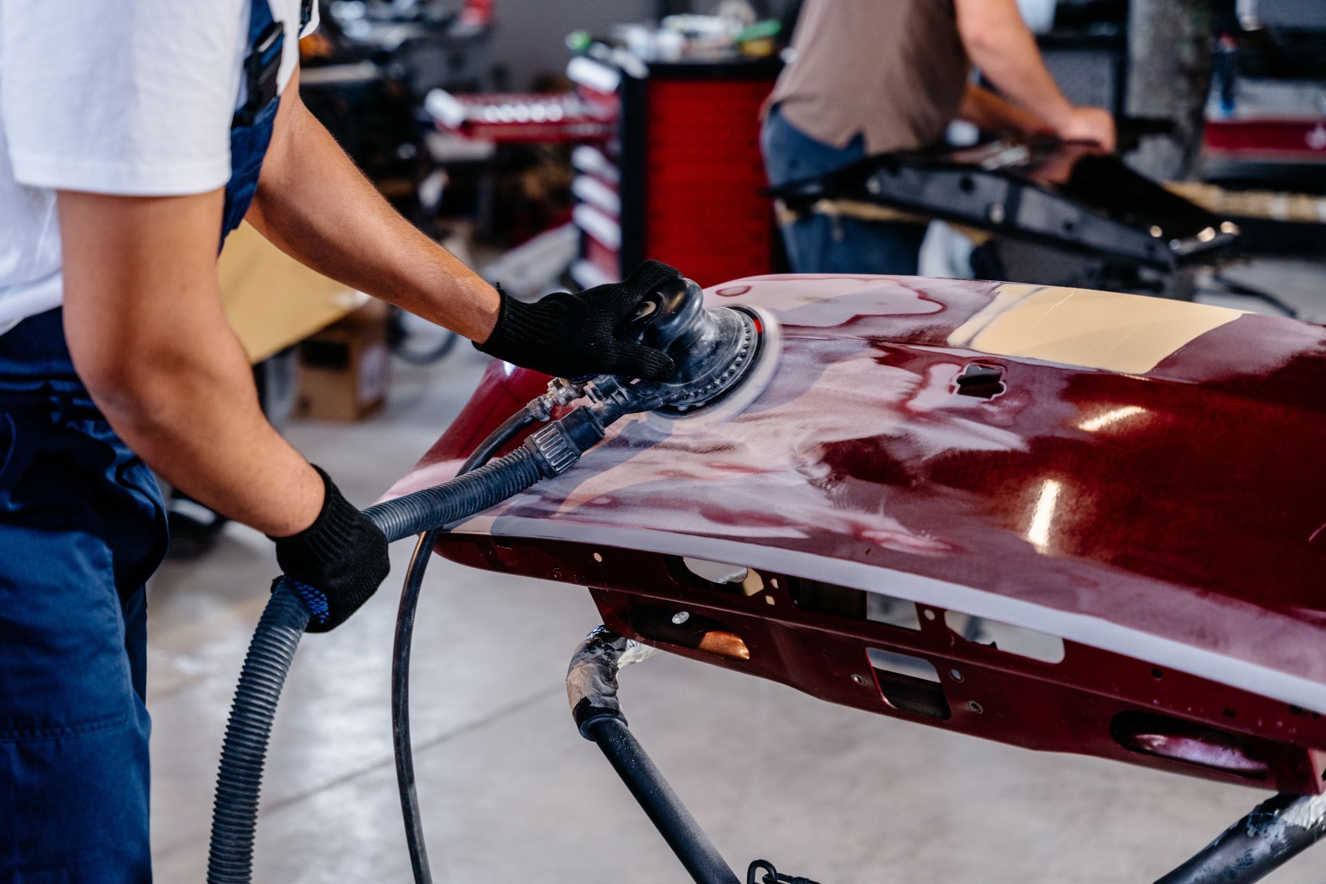 Worker polishing a red car hood in an auto body shop