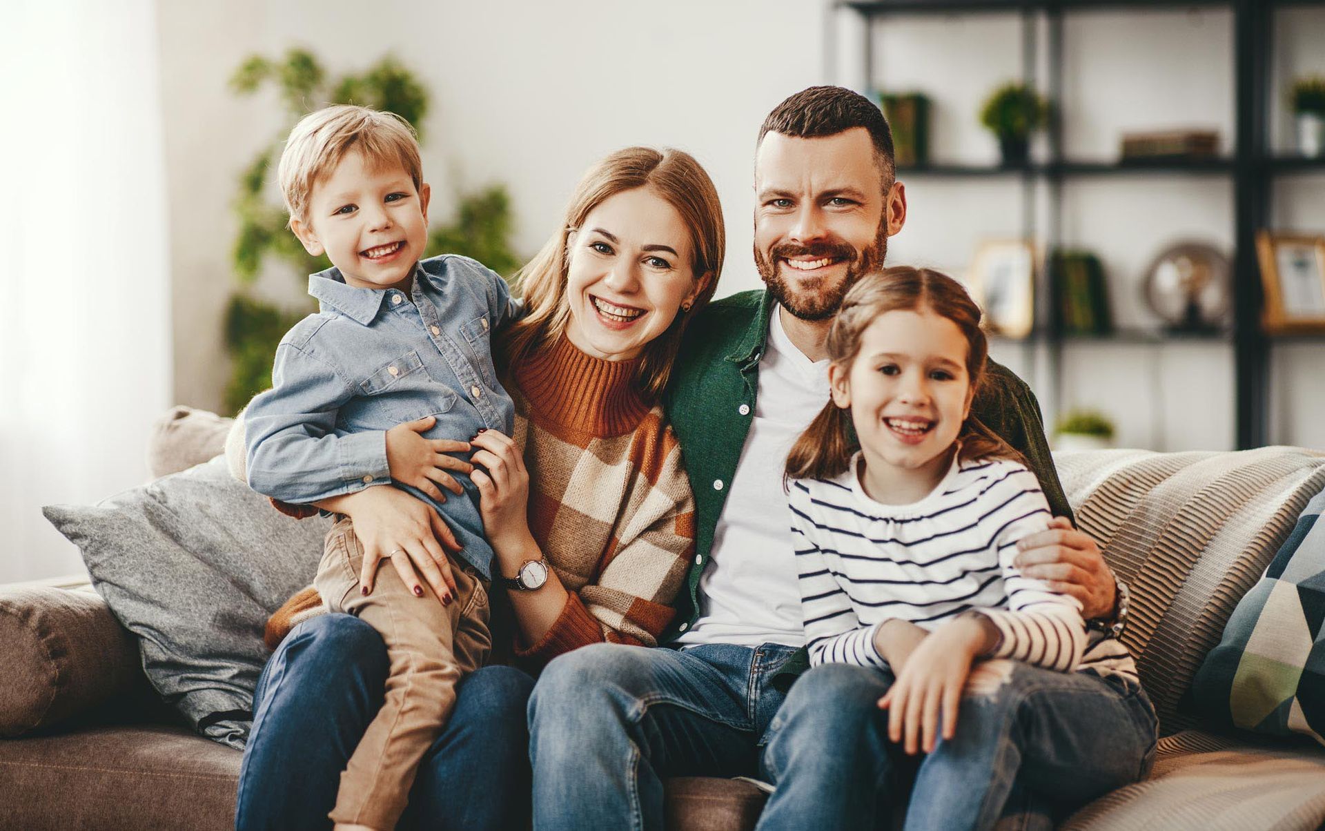 Family of four smiling and sitting on a couch in a living room.