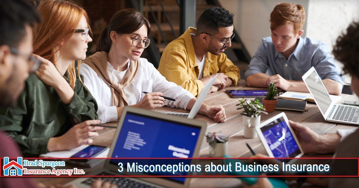 A group of diverse professionals collaborates at a wooden table with laptops and documents, discussing business insurance.