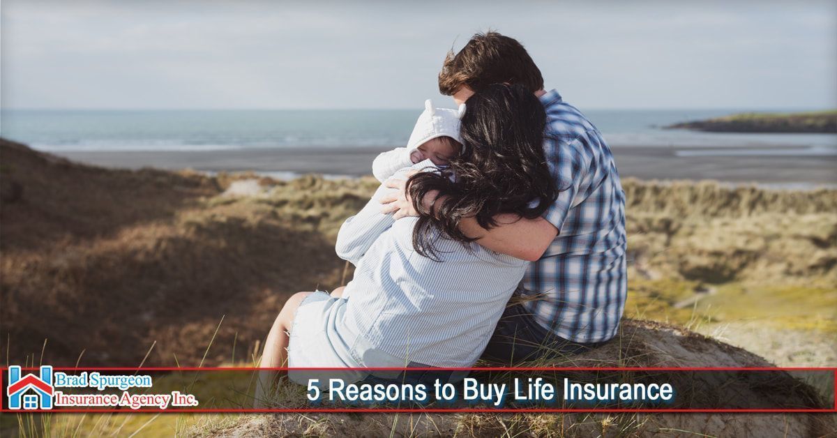 A couple embraces a small child on a sandy hill overlooking the ocean