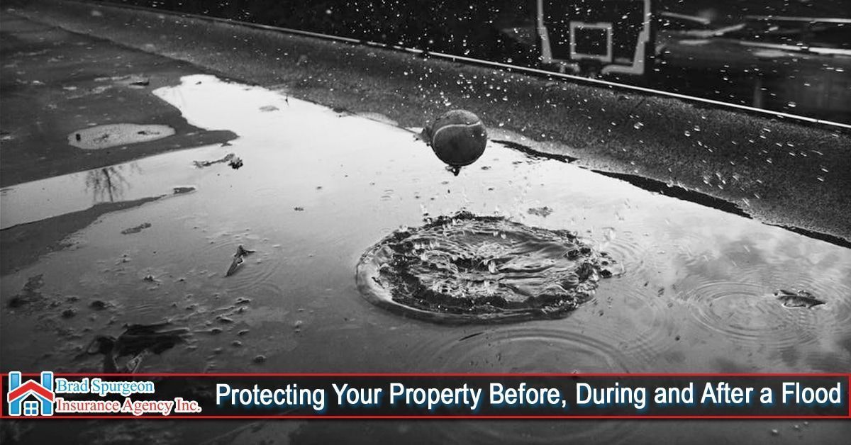 A raindrop splashes into a puddle on a paved driveway with a basketball hoop in the background