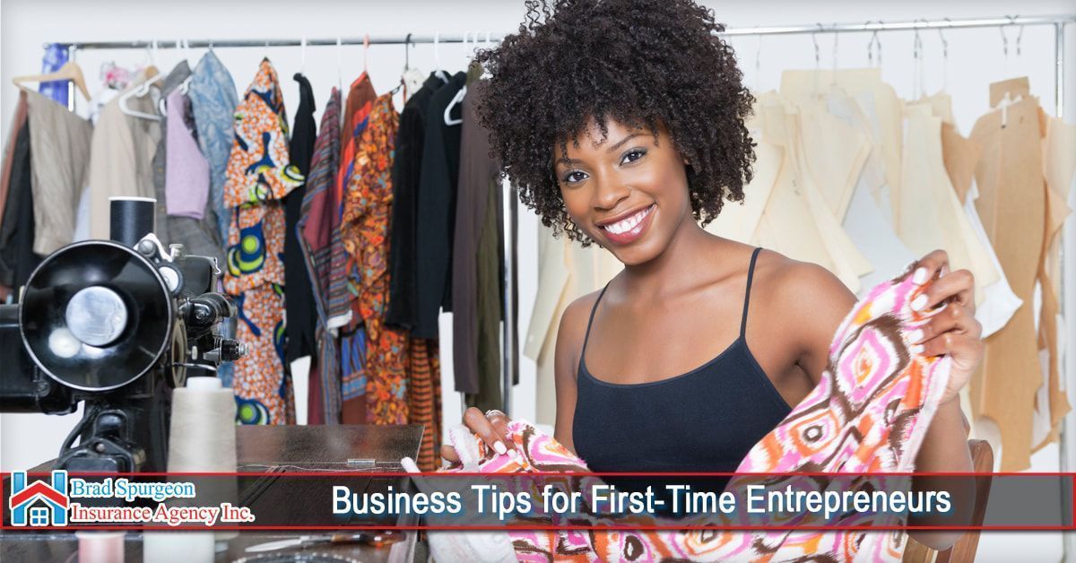 A smiling fashion designer holds a piece of patterned fabric in a studio filled with clothing racks and a sewing machine.