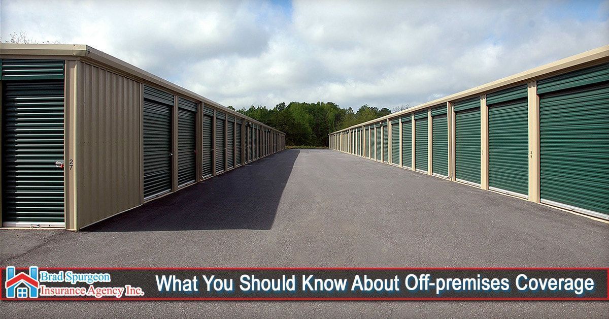 Two rows of tan and green storage units facing each other across a gravel drive under a cloudy sky.