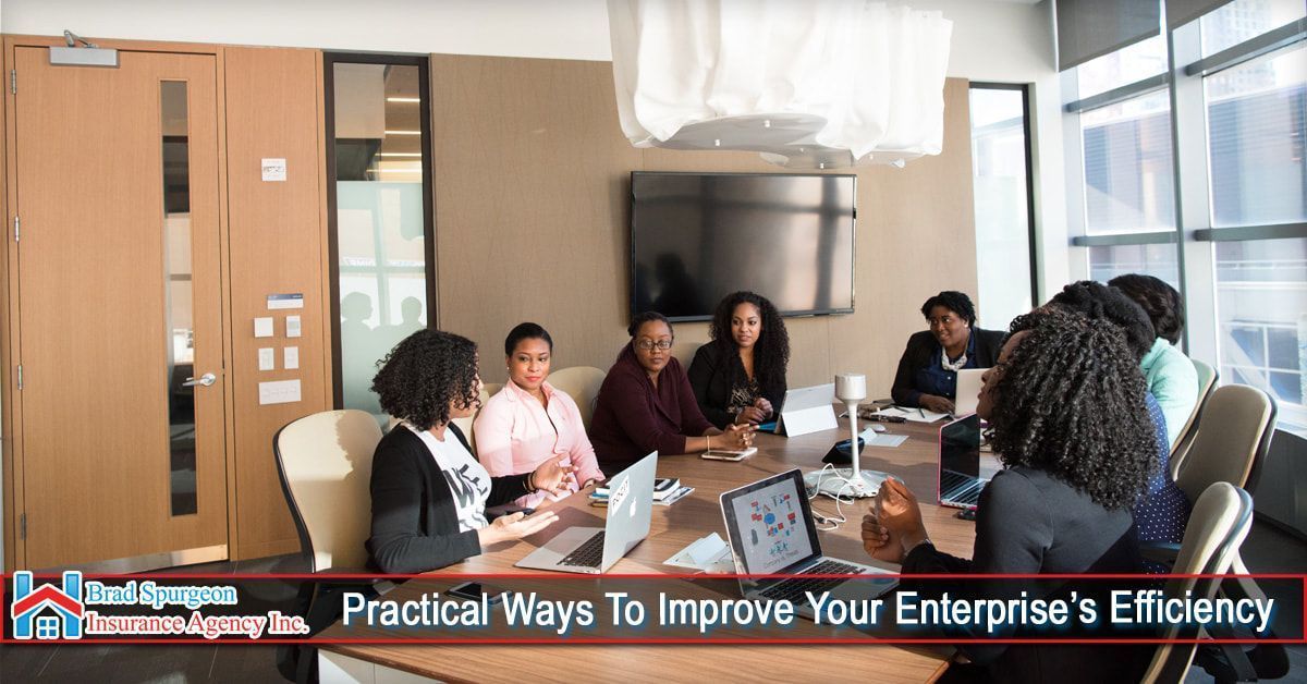 A diverse group of people sitting around a conference table in an office, using laptops for a meeting.