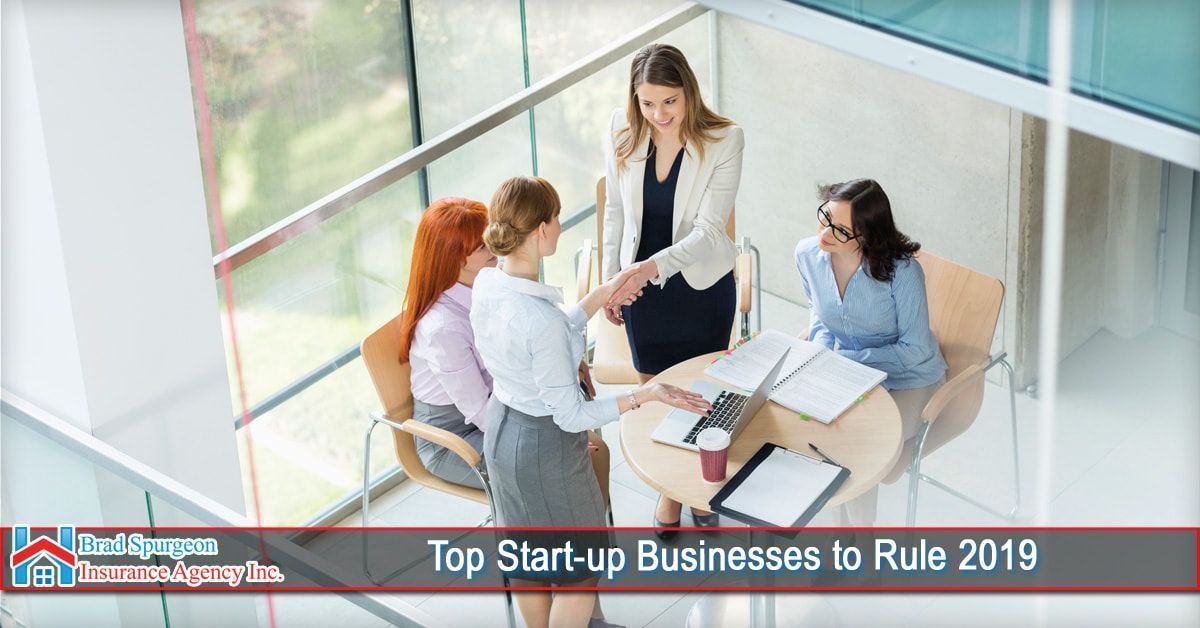 Four professional individuals in business attire shaking hands around a table in a modern, sunlit office.