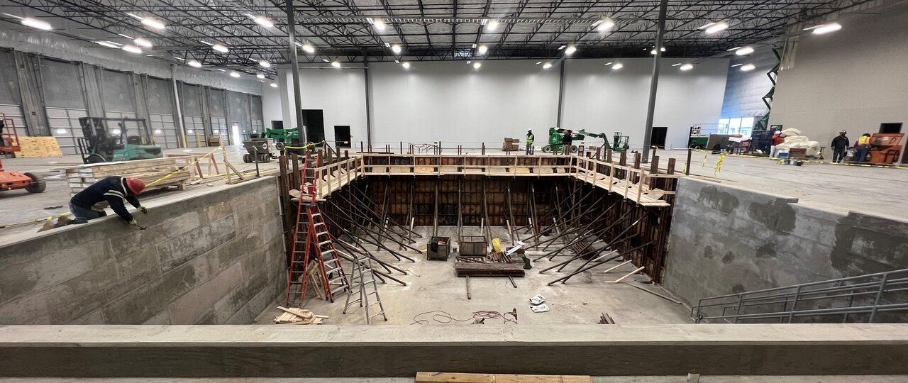 A large concrete scout pit pool is being built in a large warehouse.