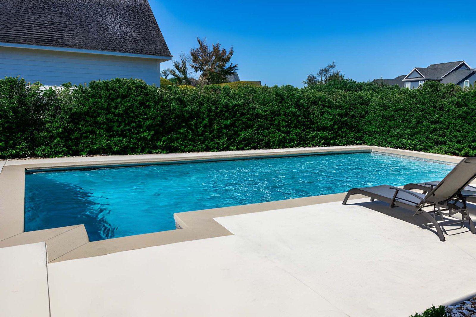 Backyard swimming pool with lounge chairs, blue water, and white patio decking