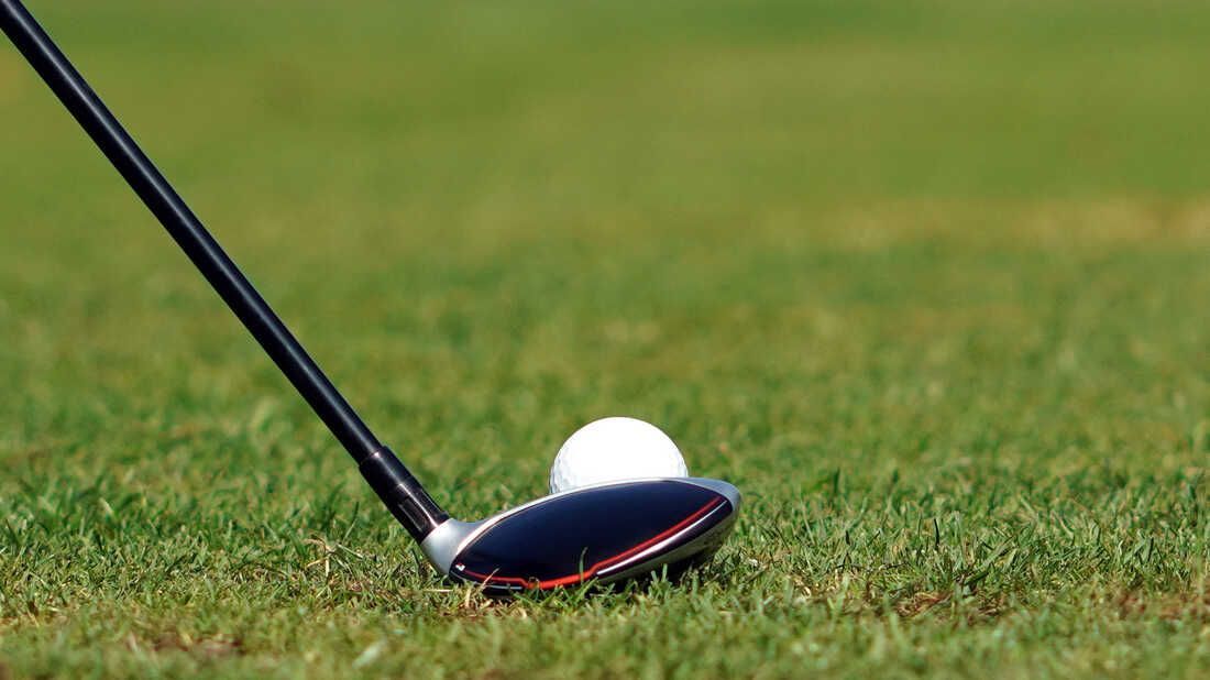 A golf club is hitting a golf ball on a golf course.