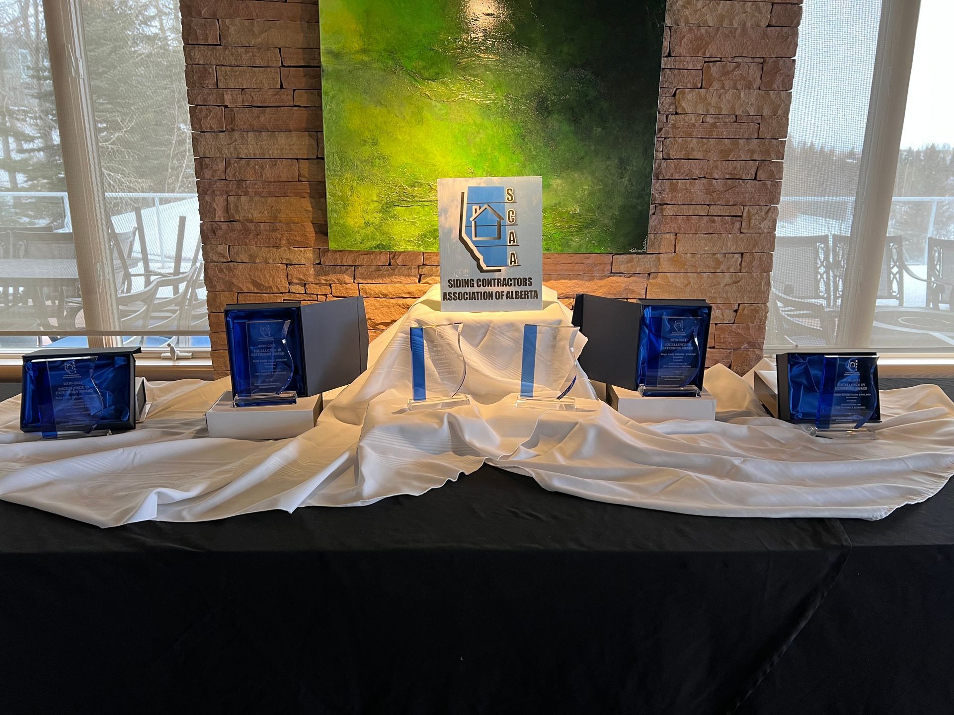 A table with a lot of trophies on it in front of a painting.
