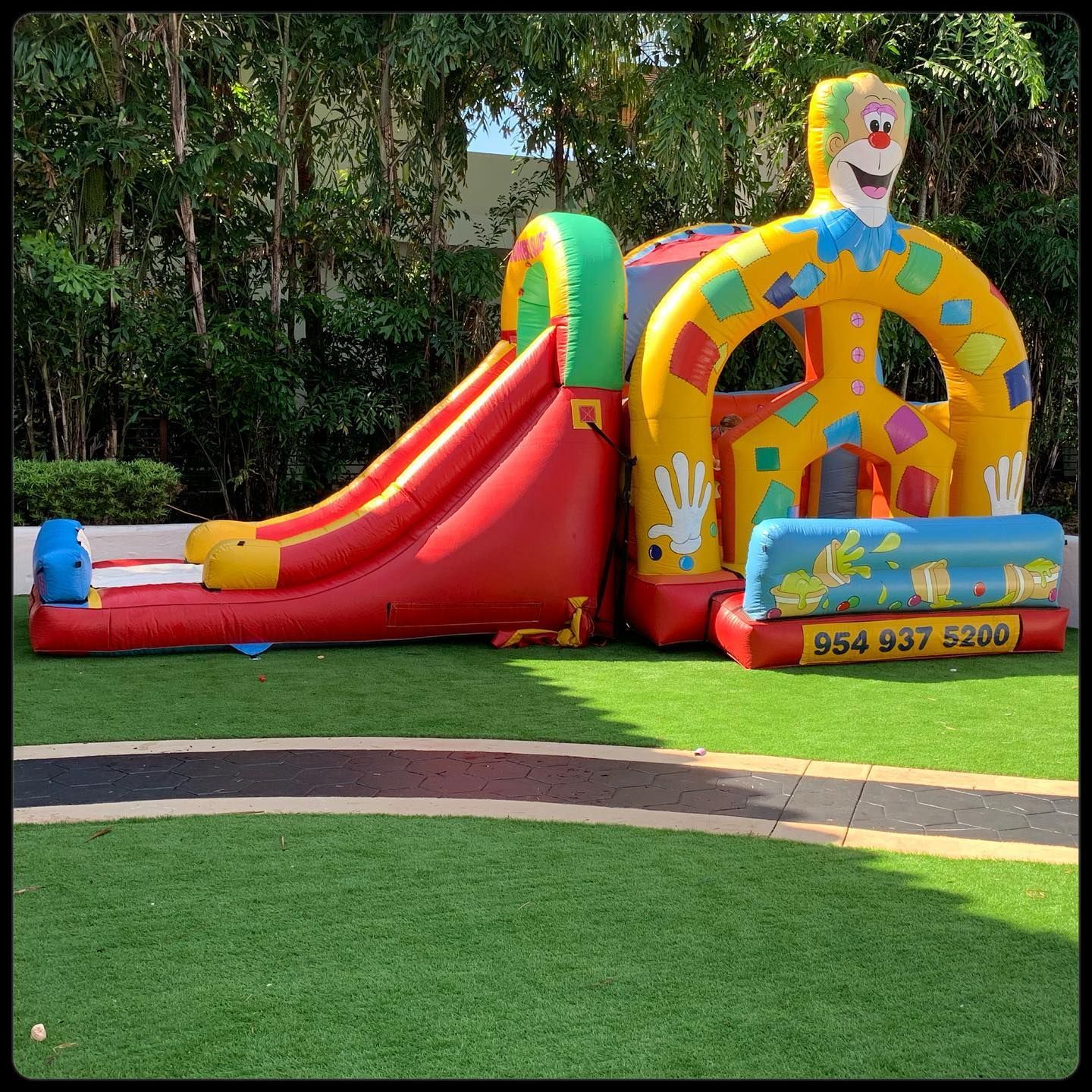 Colorful inflatable slide and playhouse with clown face in a grassy outdoor park area