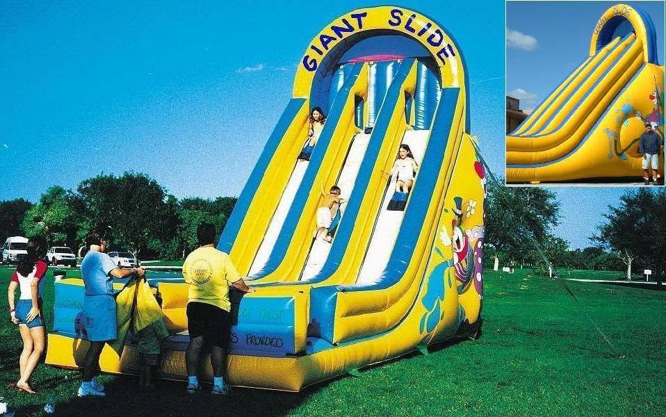 People inflating a yellow-and-blue giant slide on a grassy field, with a slide inset on the right