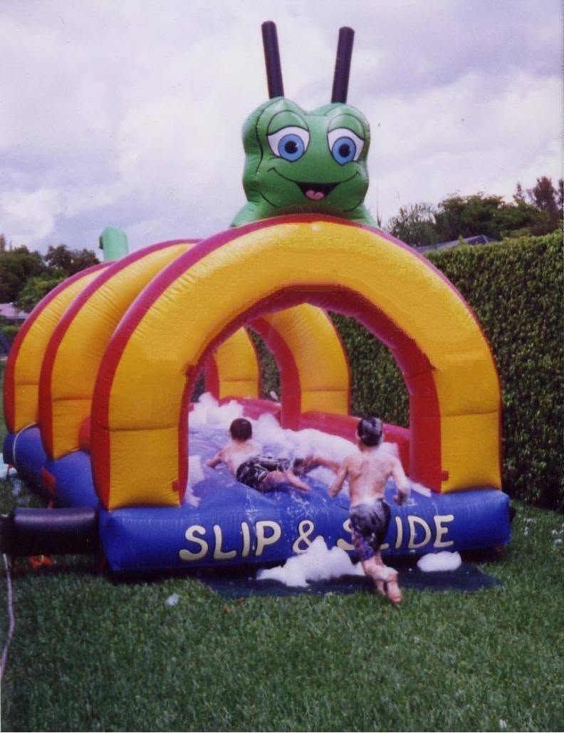 Colorful inflatable slide with a green caterpillar top, children climbing on it in a grassy yard.