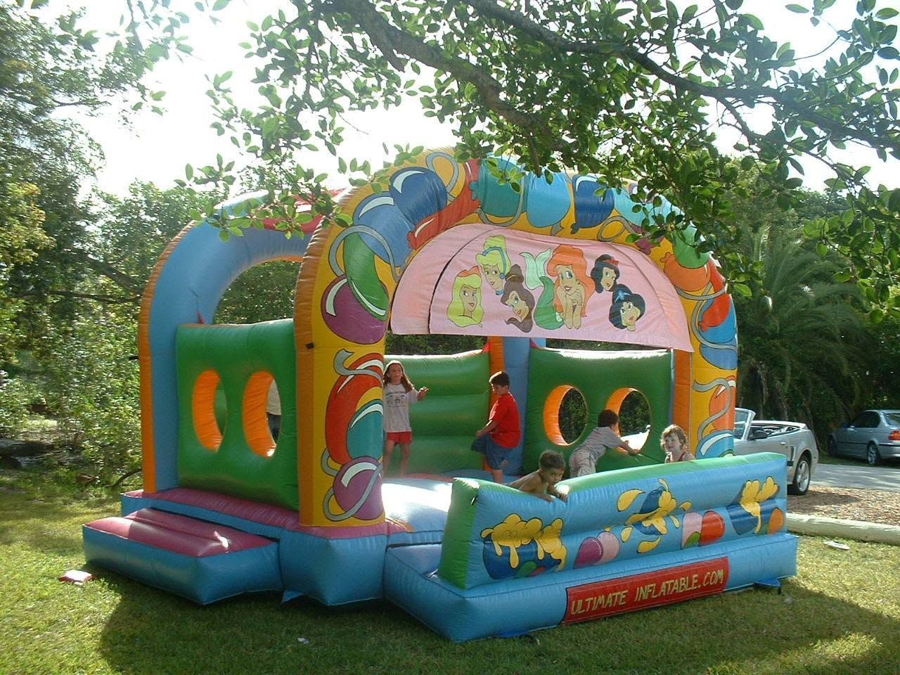 Colorful inflatable bounce house with cartoon princess graphics in a leafy outdoor park setting