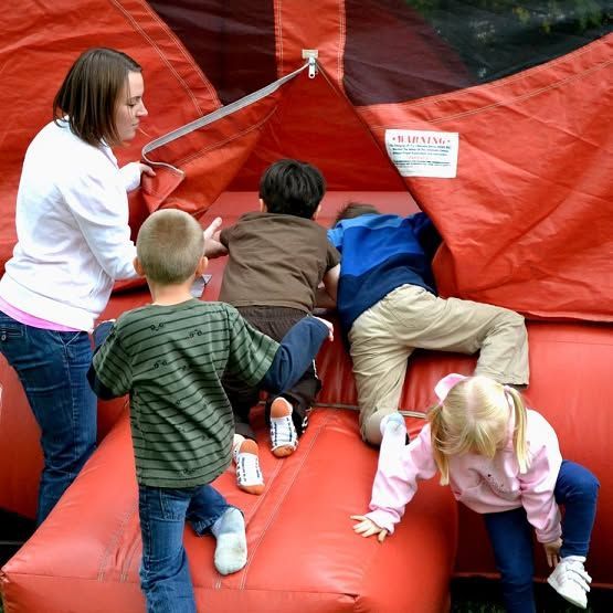 Children climbing on a red inflatable play structure while an adult stands nearby